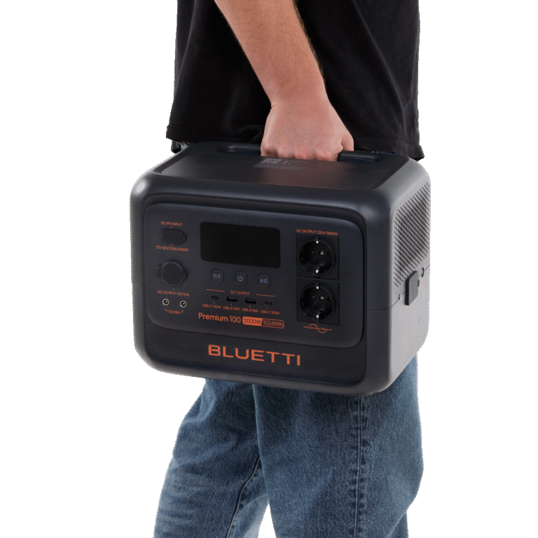 Bluetti Premium 100 portable power station in black and grey with orange accents, carried by a person wearing a black T-shirt and blue jeans, showing various ports and displays on the front.