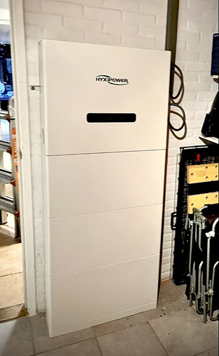 Hyxipower witte omvormer en thuisbatterij unit geïnstalleerd tegen witte bakstenen muur in technische ruimte naast gereedschap.