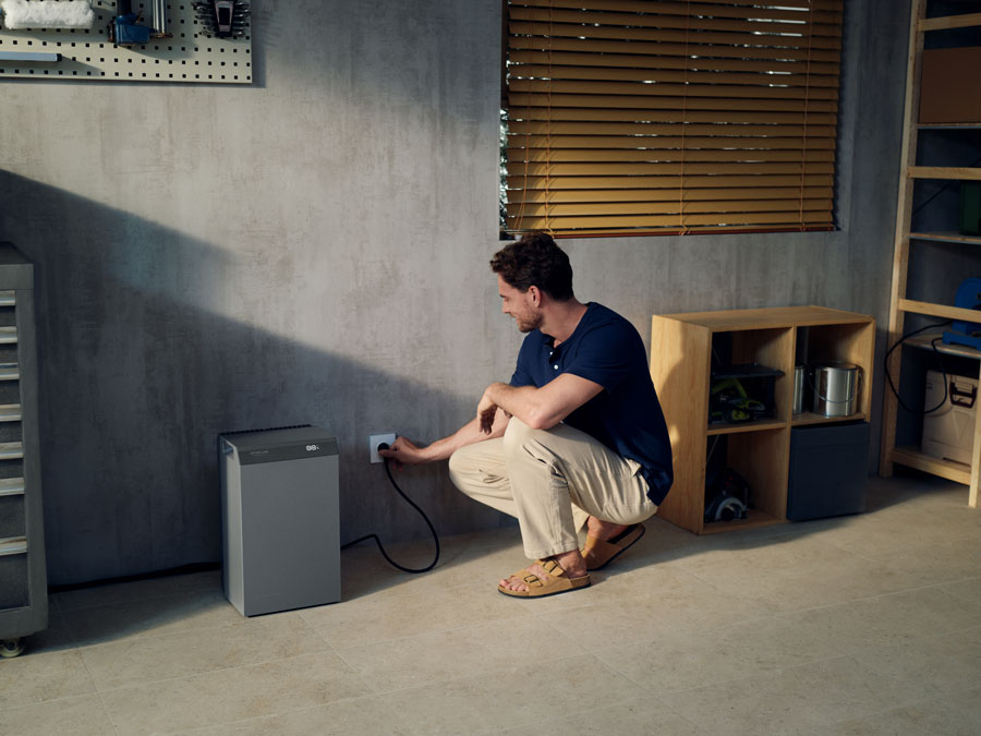 Portable power station (gray model) in a garage with a man plugging it into an outlet; compact design suitable for off-grid power supply